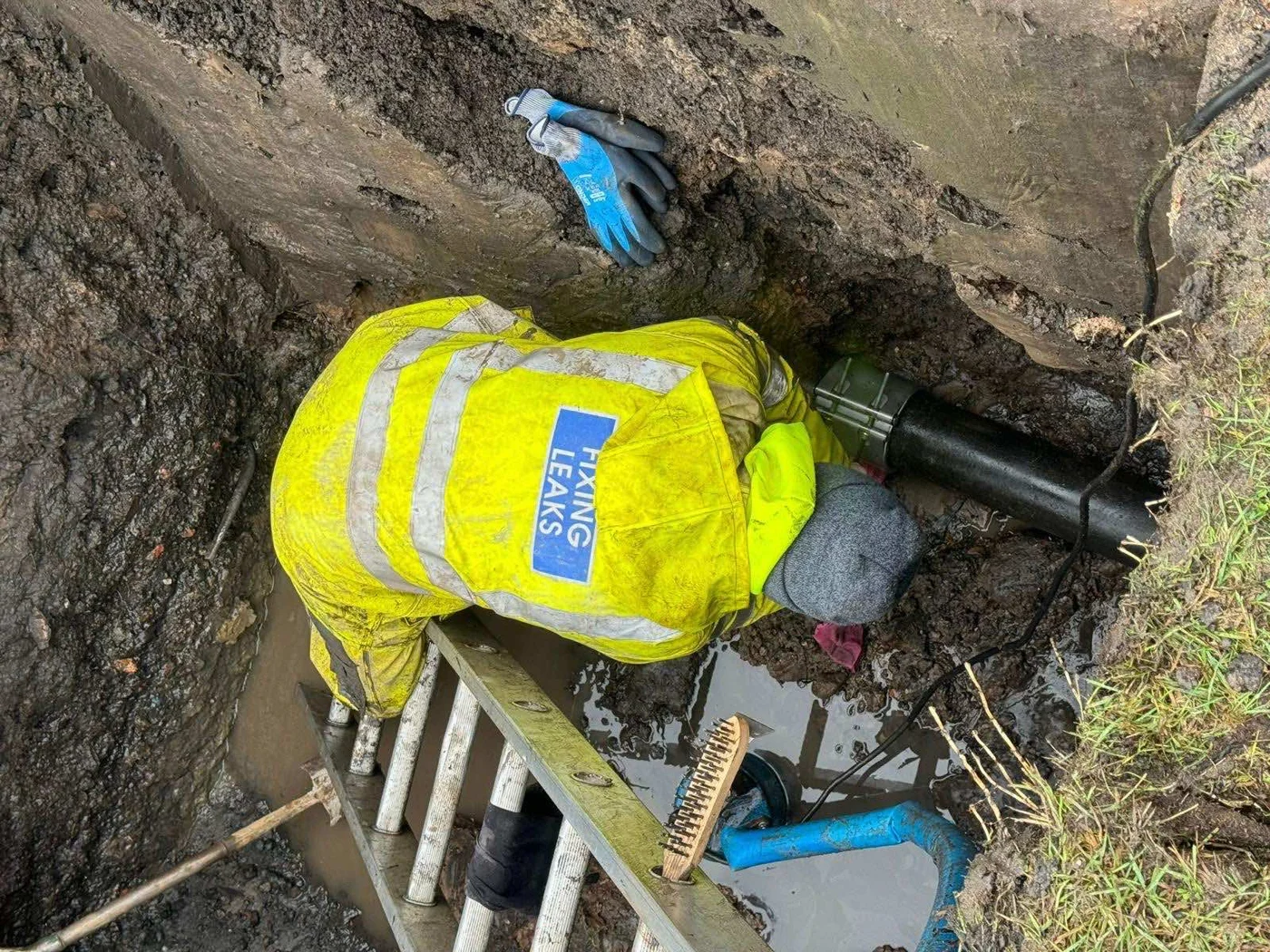 Engineer in high-visibility clothing working on exposed pipework in an excavation