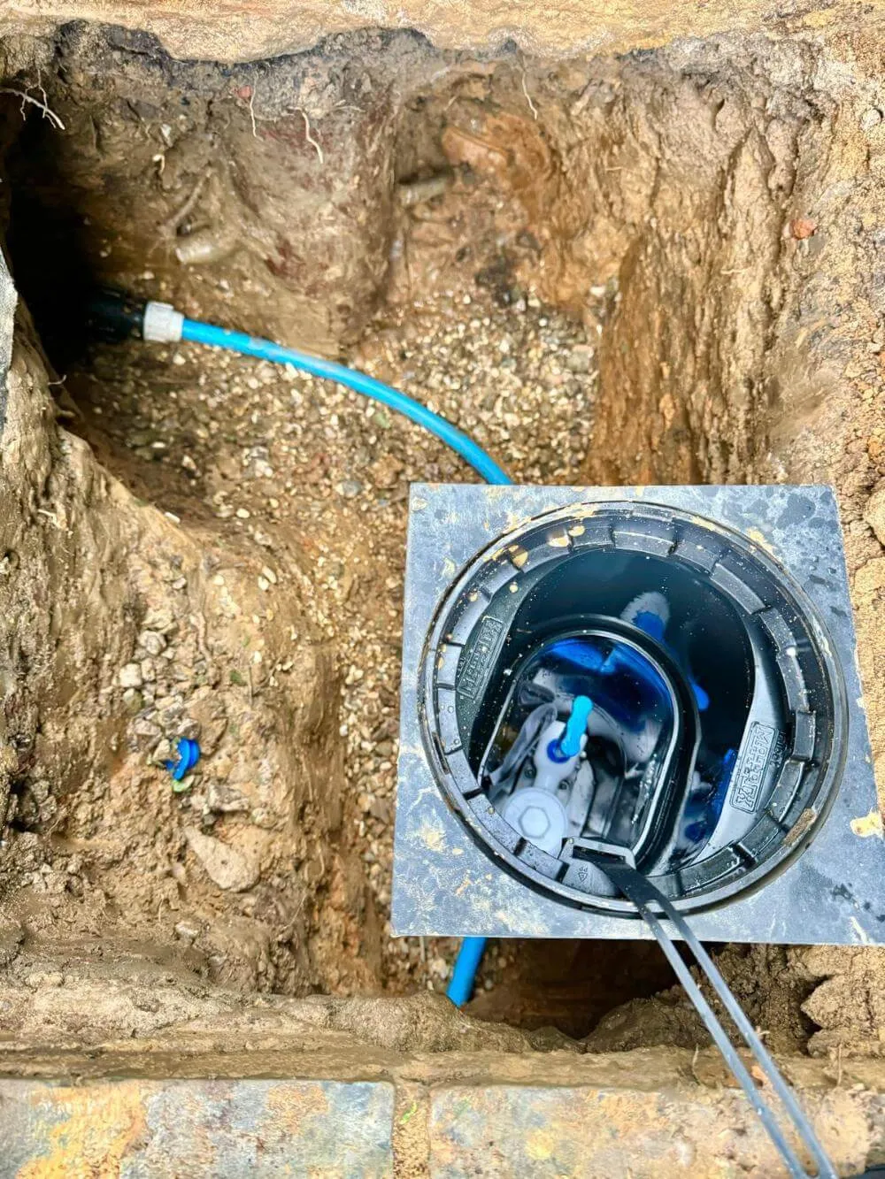 Blue water supply pipe connected to an access chamber in an excavation