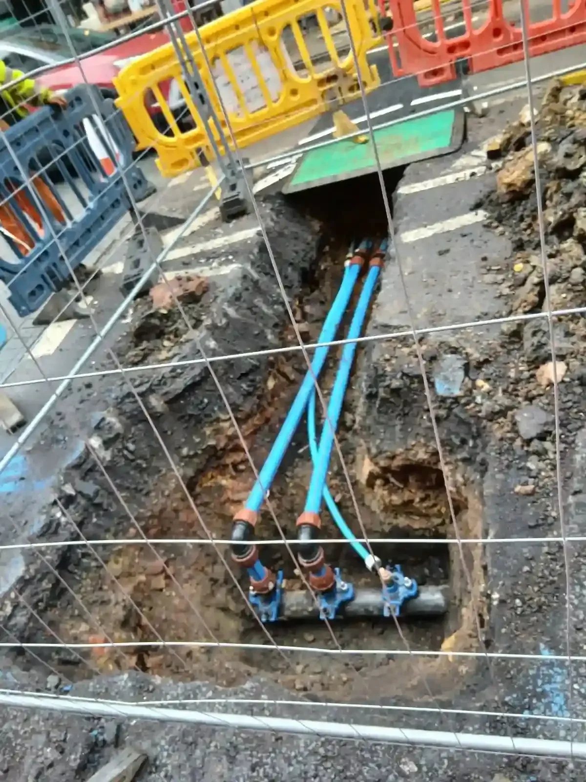 Blue water pipes and connections in a barriered road excavation