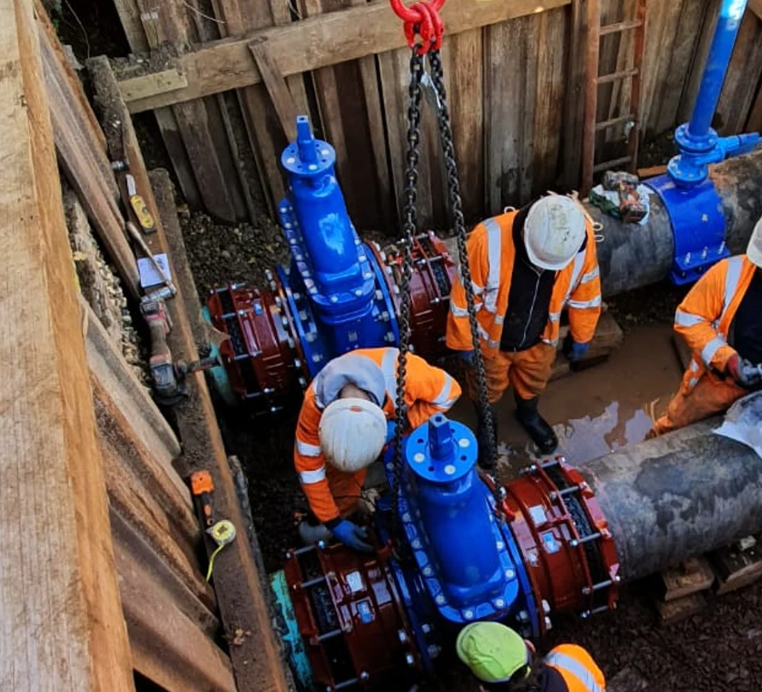 Engineers fitting large blue water valves in a supported excavation