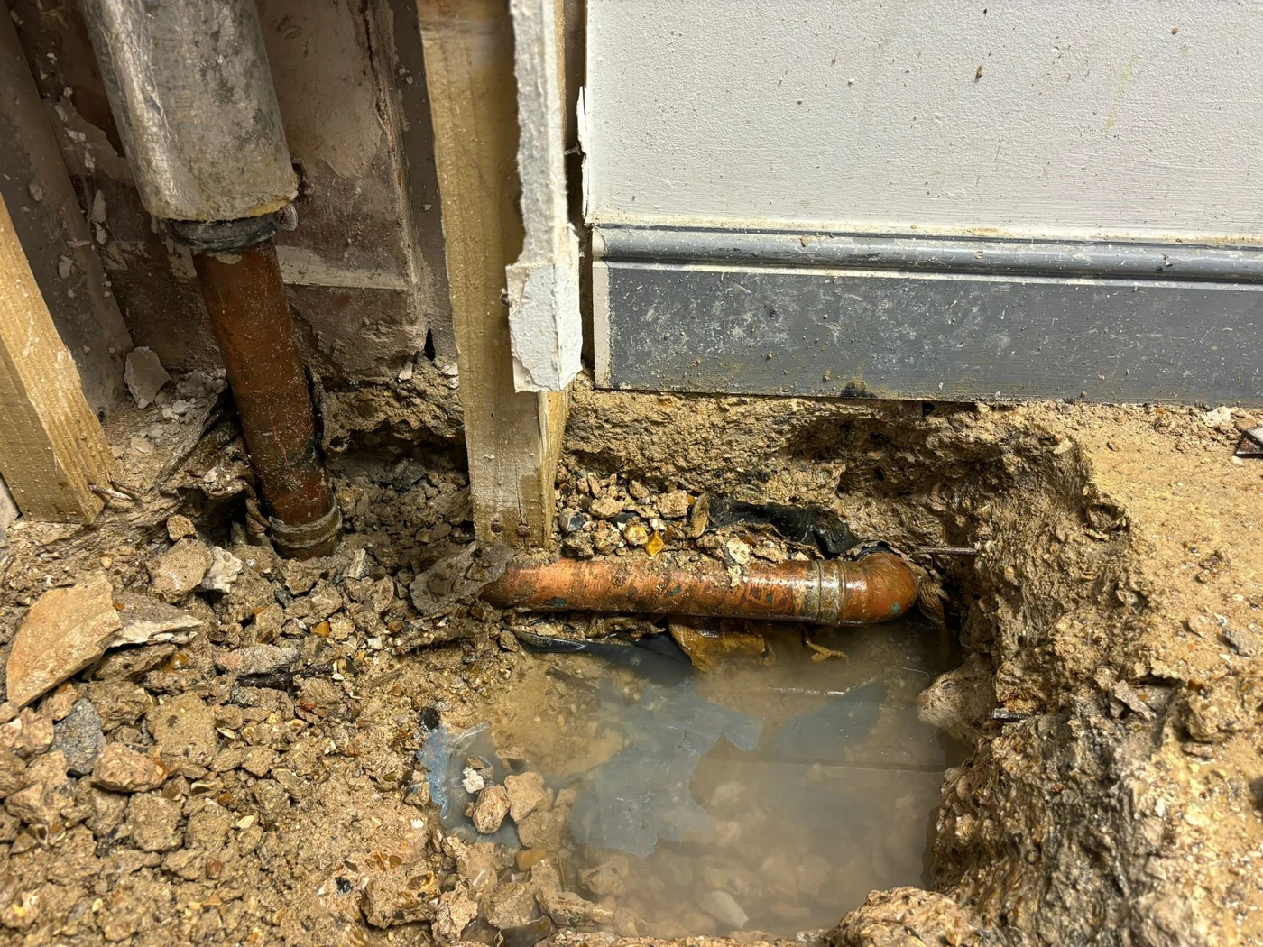 Exposed pipe and elbow beside a wall at floor level