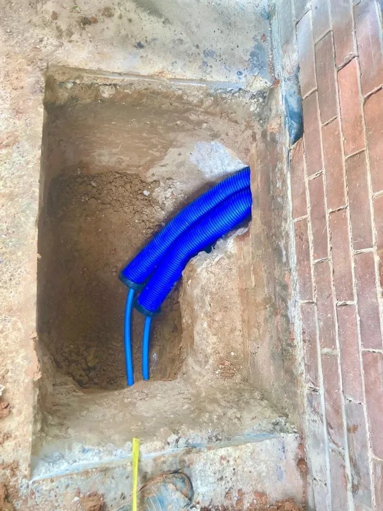 New blue pipework routed through an excavation alongside a wall.