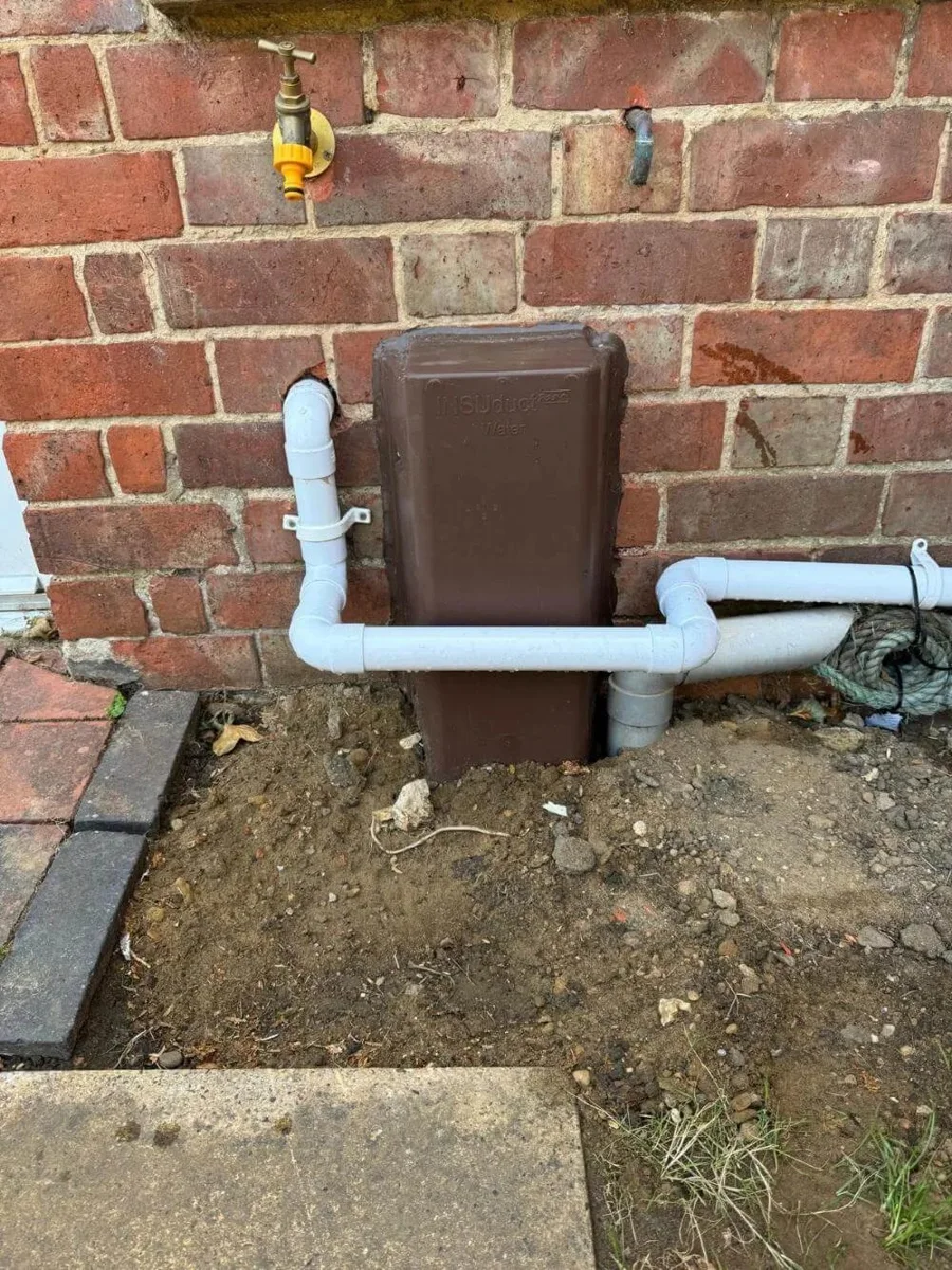 Protected pipework routed into a property through an external wall.