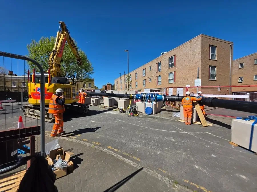 A street works team with lifting equipment and a large water main.