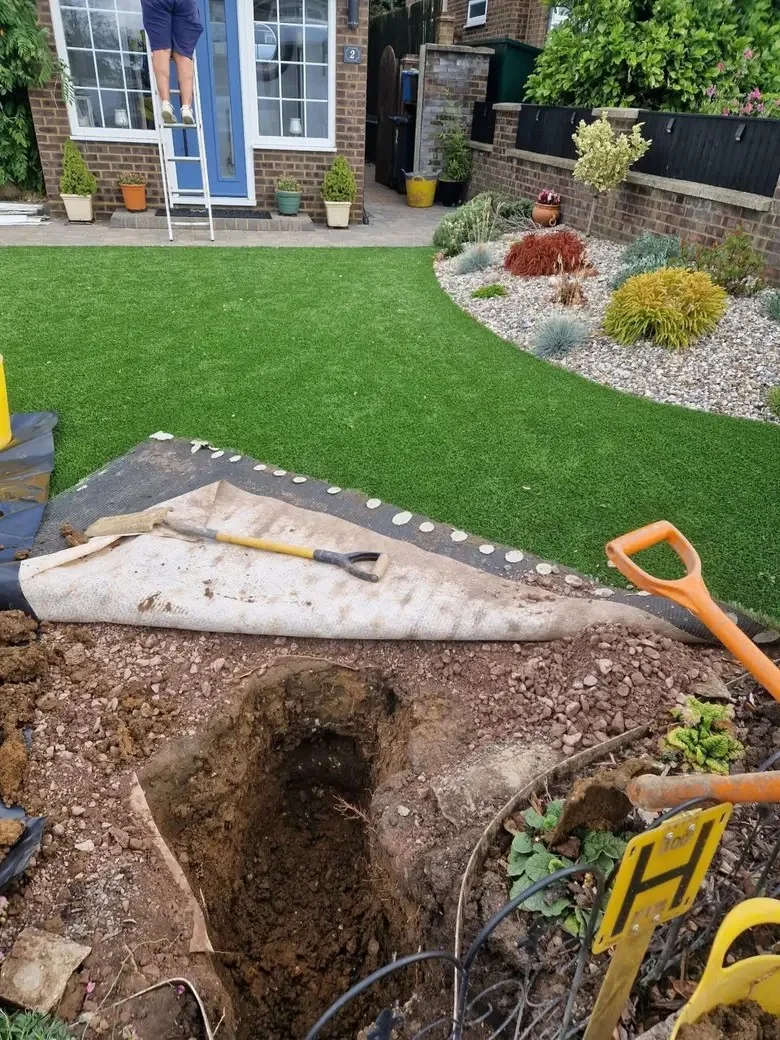 Turf rolled back beside an excavation in a landscaped garden.