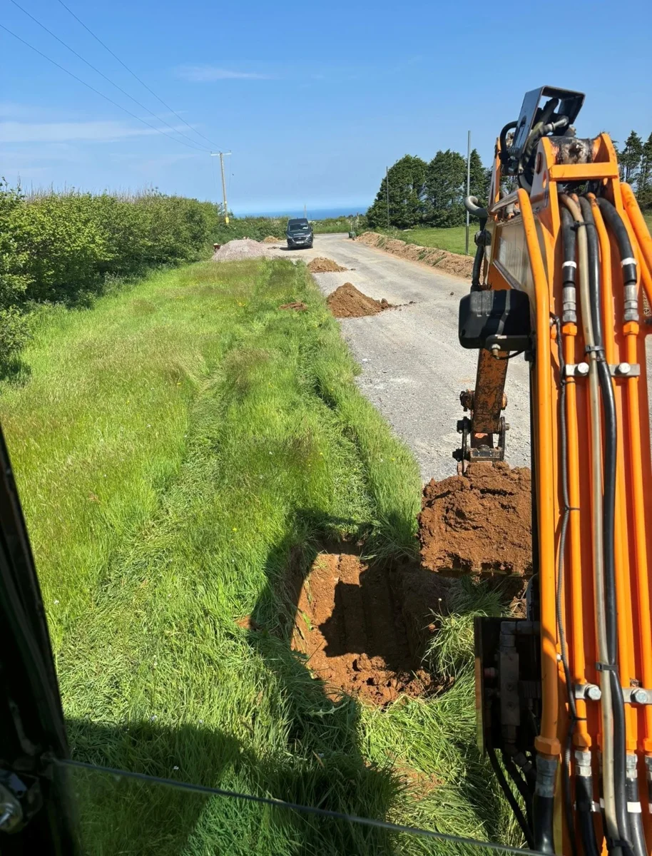 An excavator working along a narrow route beside a lane.