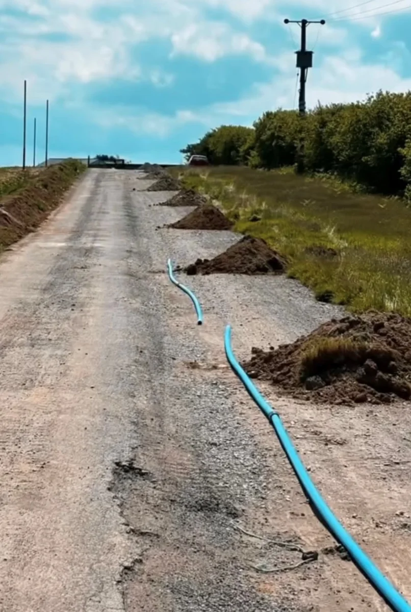 Blue pipe laid beside localised excavations along a rural access road.