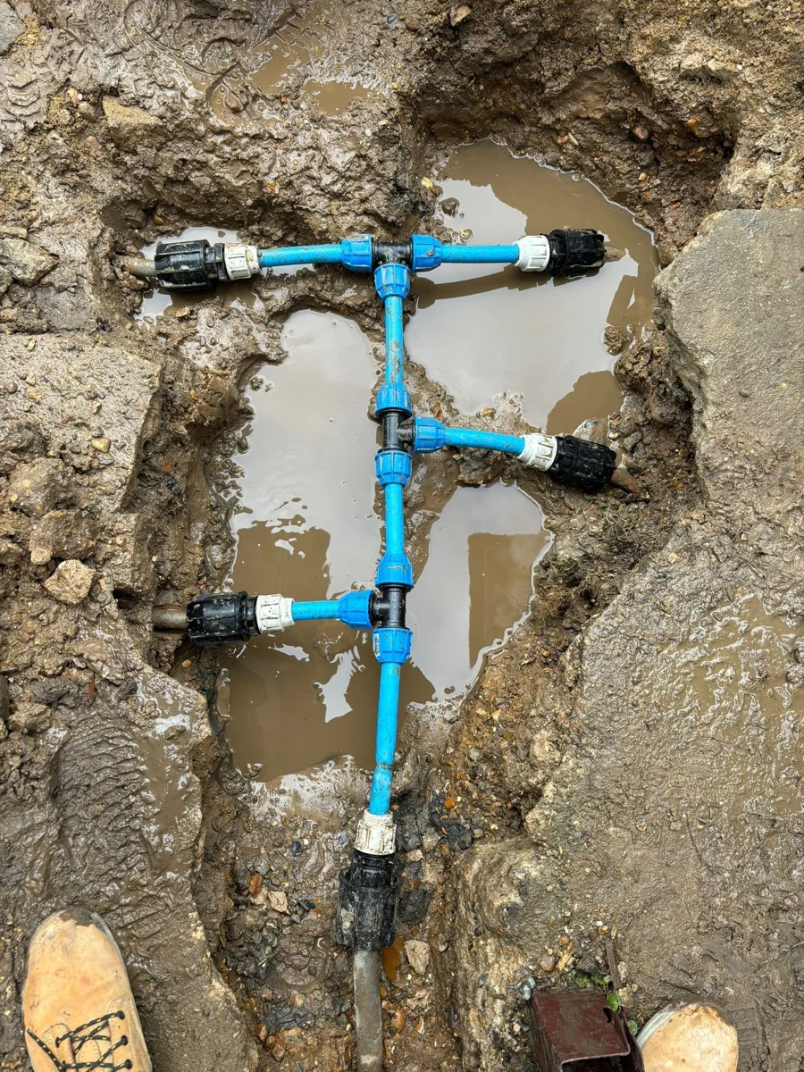 A branched blue pipe assembly within an excavation.