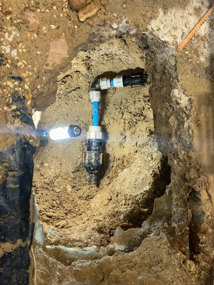 Blue pipe and compression fittings within a small excavation.