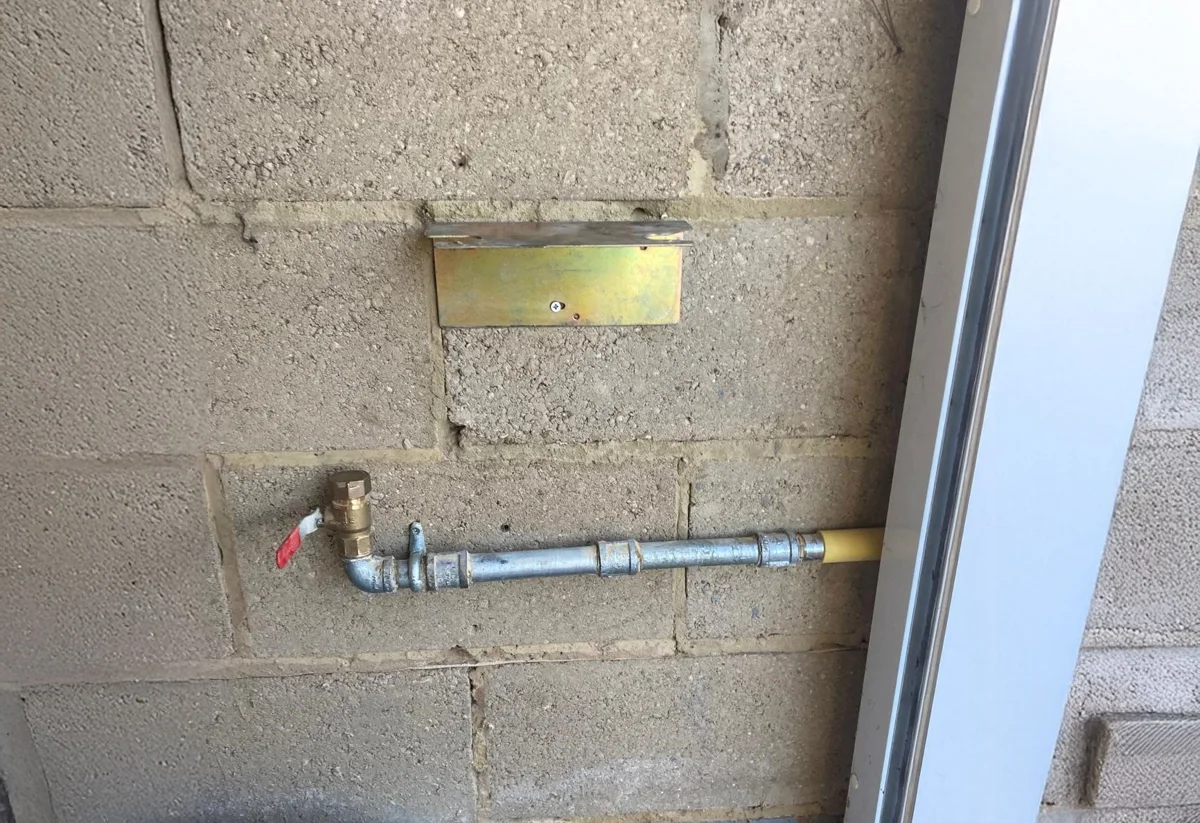 Wall-mounted metal pipework with an isolation valve.