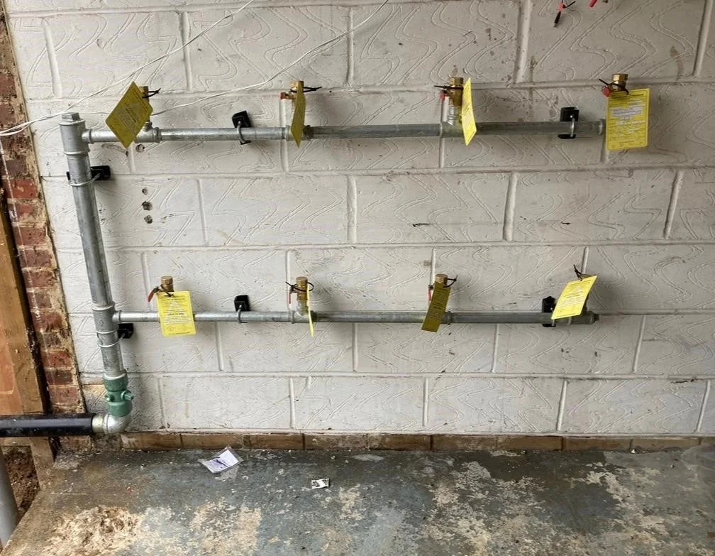 Wall-mounted pipework with multiple individually labelled valves.