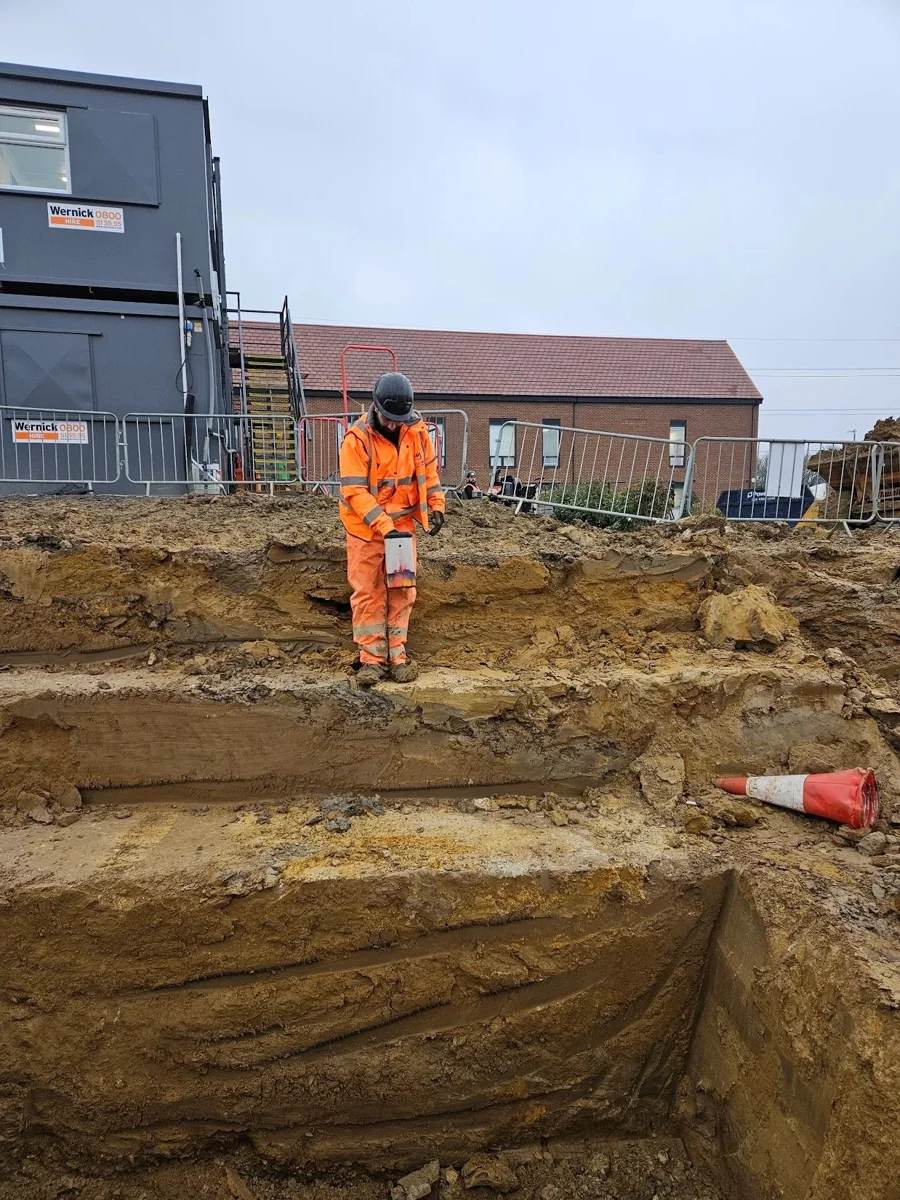 An engineer standing beside an excavated route outside a commercial building.