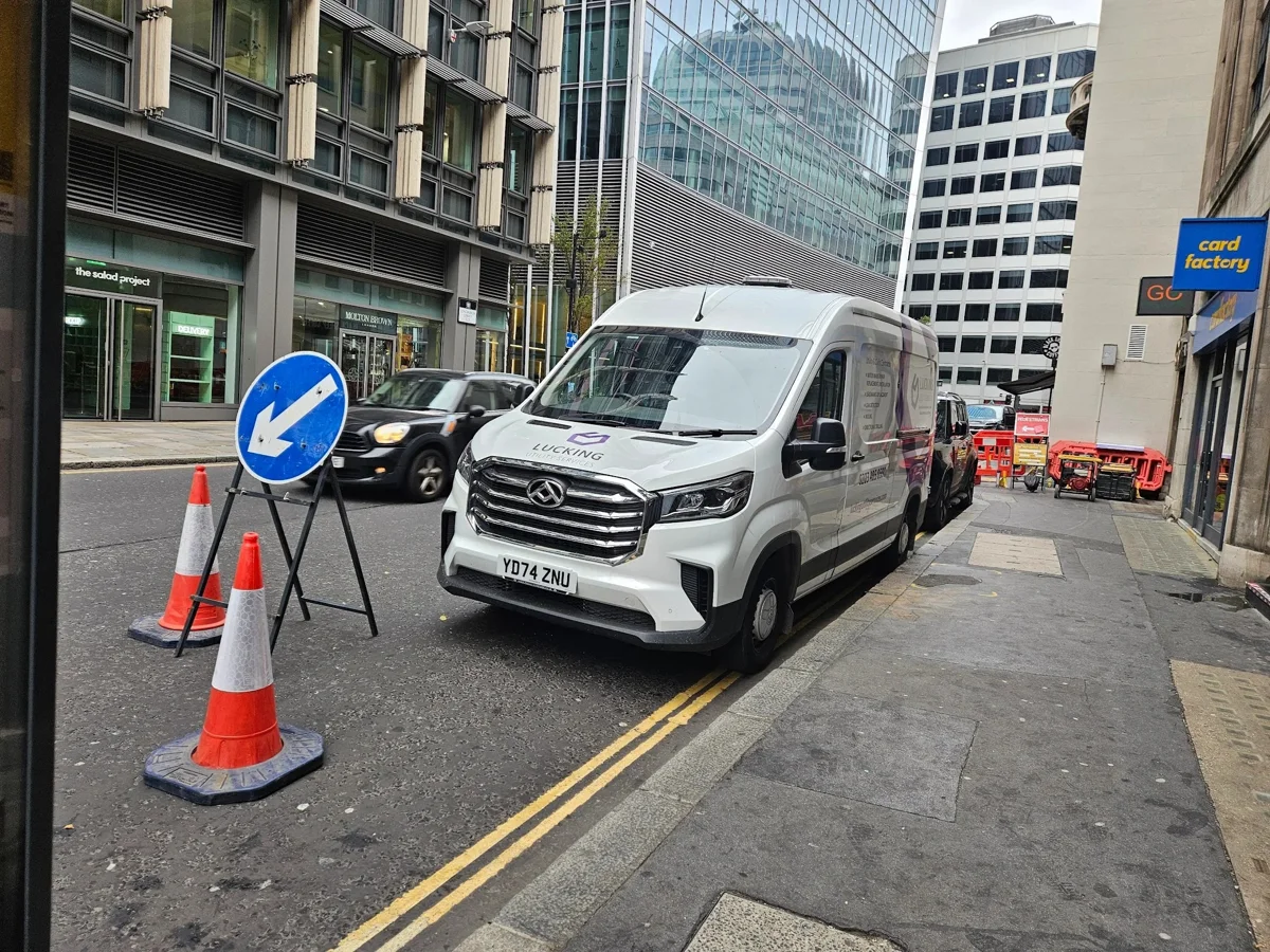 A Lucking service van beside a marked work area in a city street.