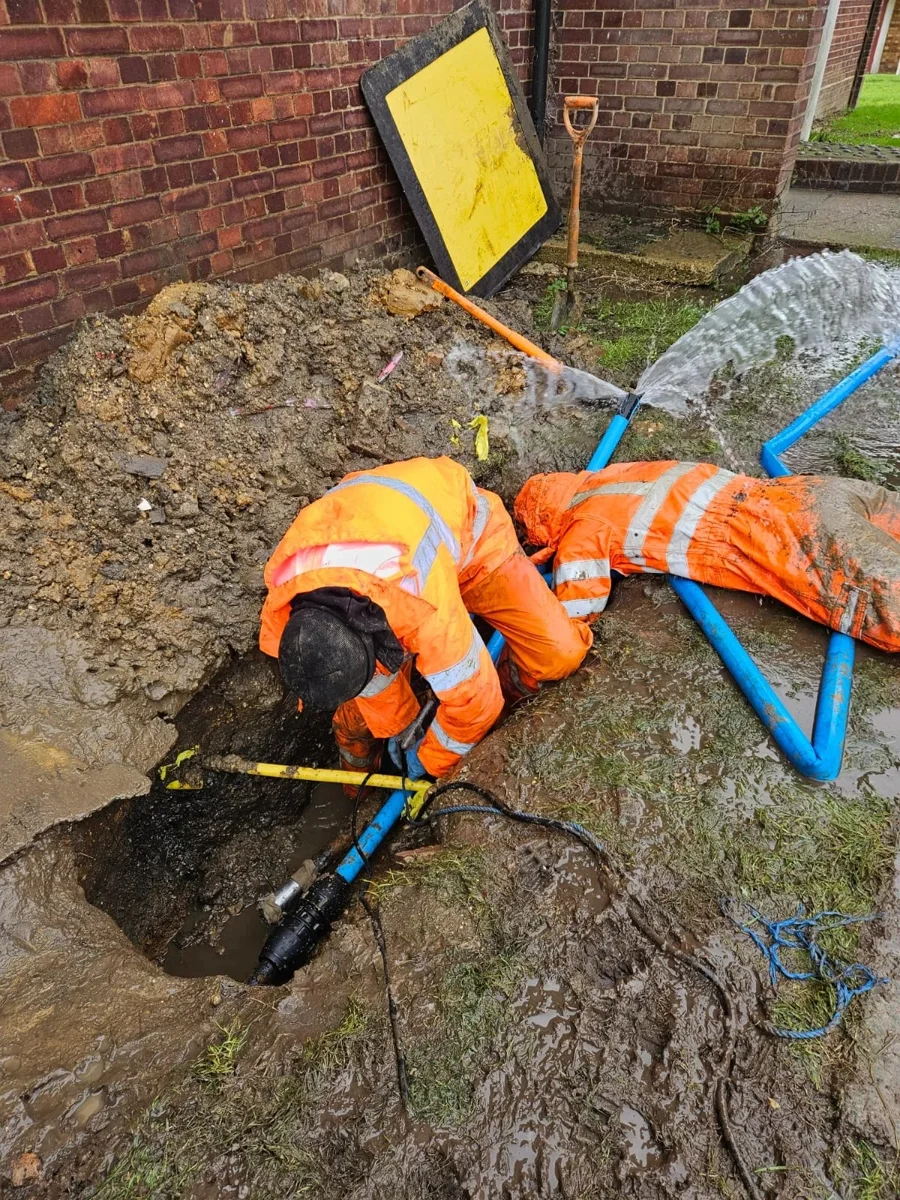 Engineers working on blue supply pipework beside a property.